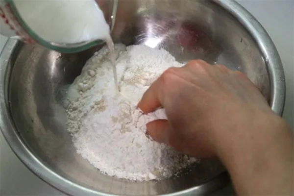 Cho bột mì và bột nở vào trộn đều sau đó từ từ cho hỗn hợp men nở vào nhào đều tay